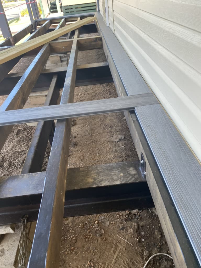 Side of a house before the job: the deck stripped back to its bare structural frame and joists